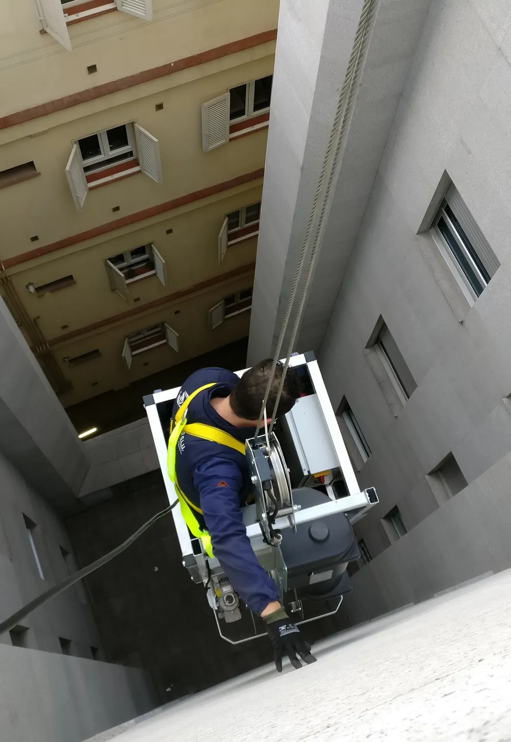 Operator in a harness descending a courtyard facade in a GPBMU cradle